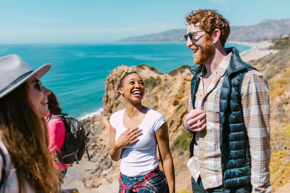Joyful friends exploring a picturesque coastal trail under the sunny sky.